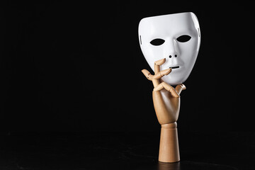 Wooden mannequin hand holding plastic mask on black background, space for text. Theatrical...