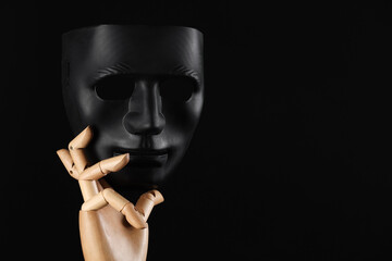 Wooden mannequin hand holding plastic mask on black background, space for text. Theatrical...