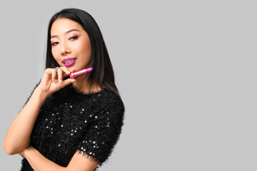 Beautiful Asian woman with lipstick on grey background