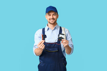 Portrait of male electrician with multimeter and wires on blue background
