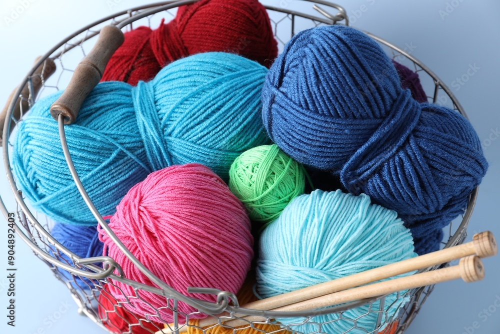 Wall mural Metal basket with bright yarns and knitting needles on light blue background, closeup