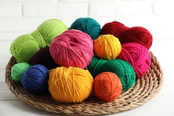 Pile of different yarns and wicker mat on white wooden table, closeup