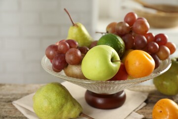 Glass vase with different fresh fruits on wooden table, closeup