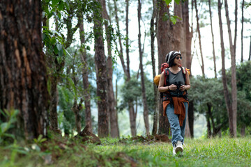 Asian female backpacker with binoculars looks at natural scenery and birds while hiking through...