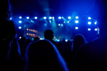 Silhouettes of spectators against a background of blue light at a concert