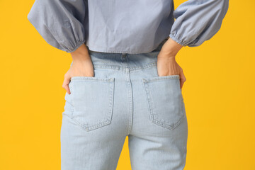 Young woman in stylish jeans on yellow background, closeup