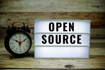 Open Source text on LED lightbox with alarm clock on wooden background