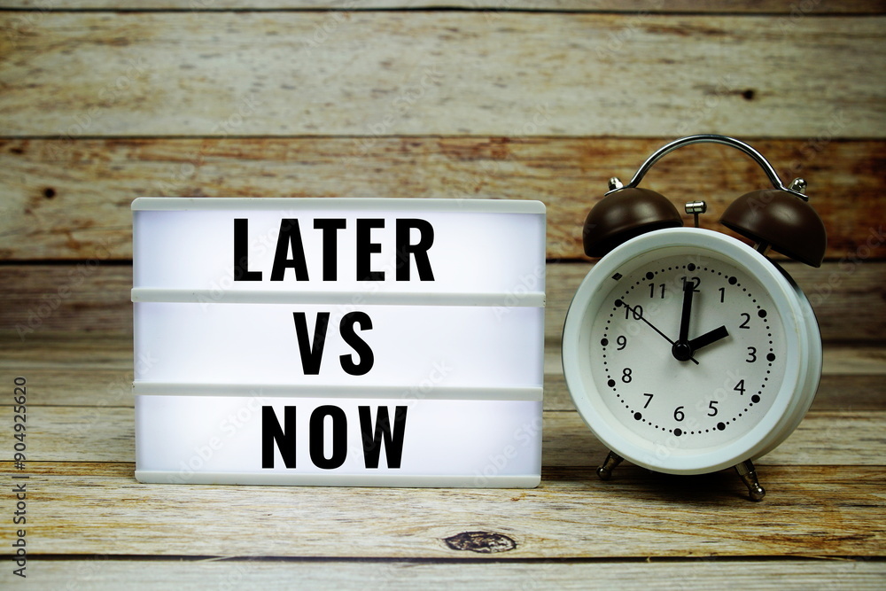 Poster later vs now text on led lightbox with alarm clock on wooden background