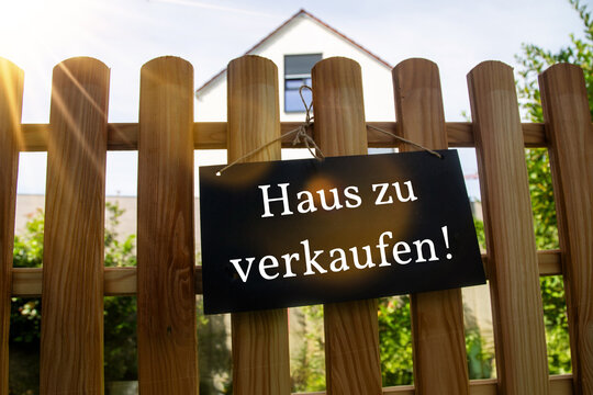 Schild mit der Aufschrift HAUS ZU VERKAUFEN an einem Holzzaun (Symbolbild)
