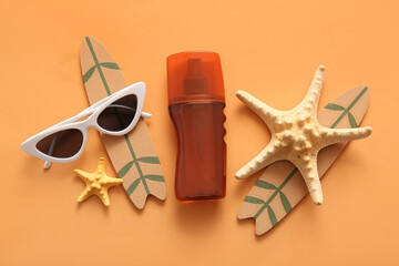 Bottle of sunscreen cream, starfishes, sunglasses and surfboards on orange background