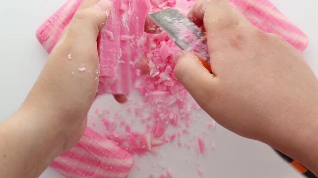 Close-up of hands cutting and crumbling pink soap bars with a knife, creating satisfying soap shards and flakes on a white surface. Part 2 of 10