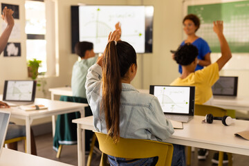 In high school, students raising hands and using laptops during classroom lesson