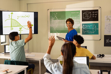 In high school, students raising hands in classroom while teacher explains math lesson