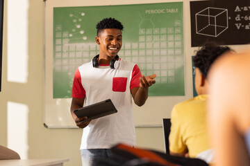 Presenting project, teenage boy with tablet smiling in high school classroom