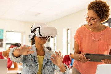 In high school, student using VR headset while teacher with tablet watching
