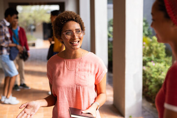 Smiling student holding book and talking with friend outside high school building