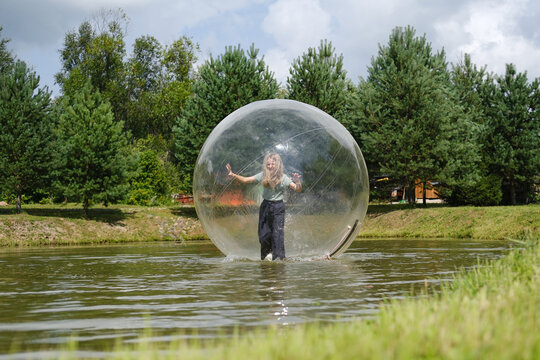 Aqua zorbing on water. A girl in a transparent balloon on the water, lake, nature, forest. Girl inside big inflatable ball having fun, summer activities