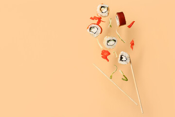 Tasty flying sushi rolls, ginger, cucumber and chopsticks on beige background