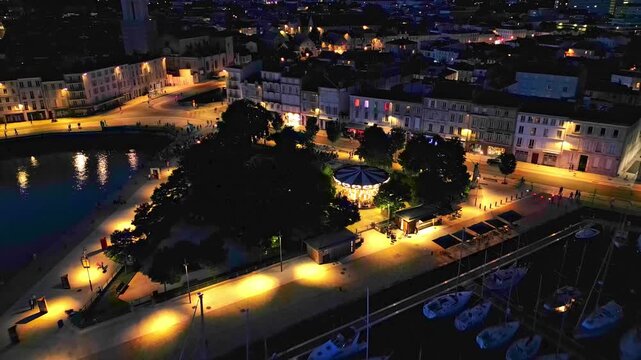 Approaching aerial movement about the Quai Valin square and carousel at night, La Rochelle, France.