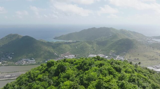 Drone view revealing Grand Case Airport on Saint Martin with beautiful hills covered with greenery in Carribean Island.