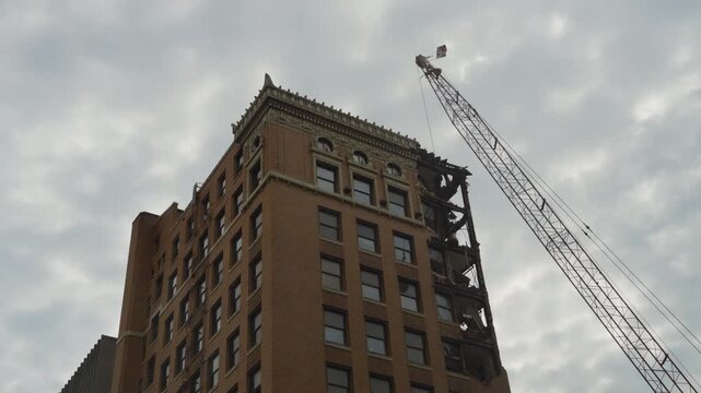 A detailed view of the demolition process of a historic high-rise building in Youngstown, Ohio. The crane with a wrecking ball is seen actively dismantling the ornate upper structure.