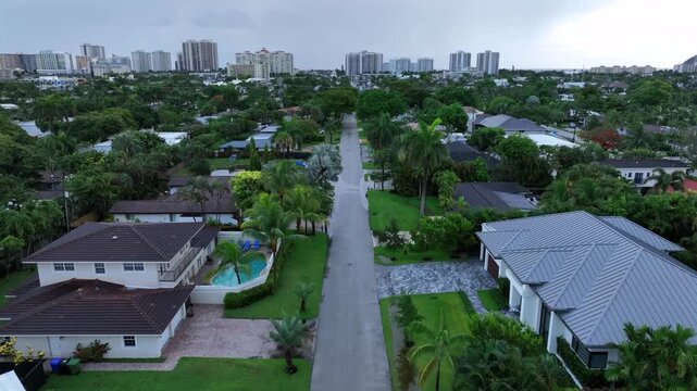 Residential neighborhood with green lawns and palm trees in Florida. High-rise buildings visible in the distance. Aerial.