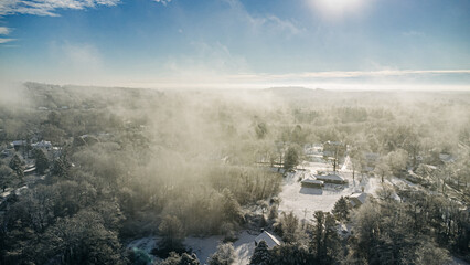 Fototapeta premium Aerial view of a foggy, snowy landscape with trees and houses