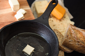 Skillet with butter, bread, and cheese on a wooden board