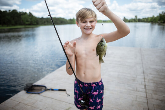 Boy on dock smiling with bluegill fish caught on line