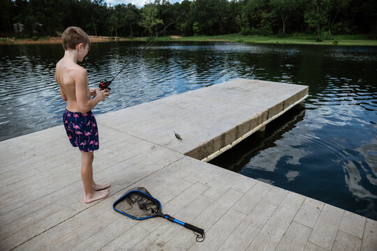 Boy reeling in small bluegill fish caught at lake