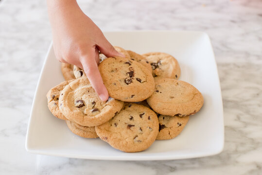 Close up of a little girls hands grabbing a chocolate chip cookie