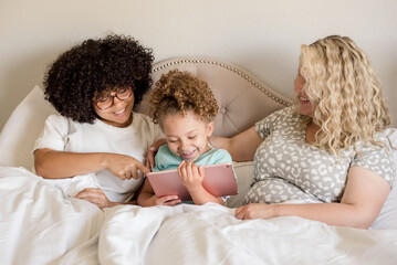 Little girl holding a tablet with mother and big sister