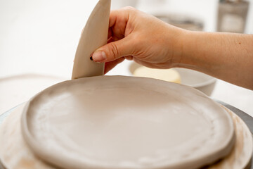 Girl is using a pottery scrapper to smooth the edges of a clay product. Crafting smooth angle conversion and textured ribs with a clay pottery scrapper.