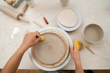 Girl is working with a sponge on a stick to shape pottery and absorb excess water from clay. Using wooden handle sponge to smooth the surface of a clay product in a pottery workshop.