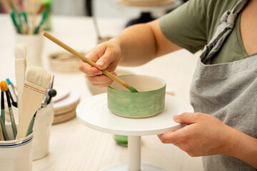 Girl is decorating a clay product with bright green color. Using a brush to paint a ceramics bowl. Learning how to paint a handmade pottery project.