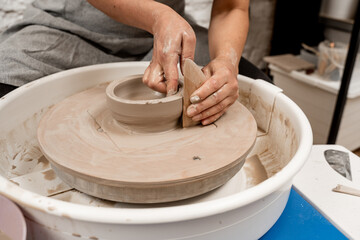 Cutting the lines on sides of a clay product with a wooden scraper. Making smooth edges of pottery with a wooden scraper and a pottery wheel.
