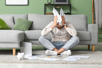 Stressed young man in debt with papers sitting on carpet at home