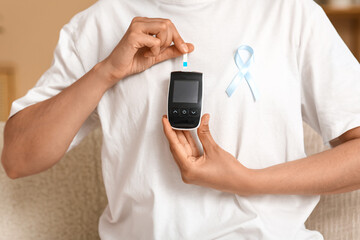 Diabetic young woman with blue awareness ribbon and glucometer at home, closeup