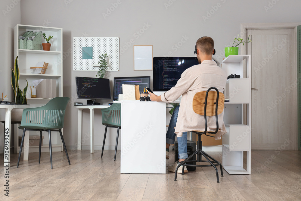 Poster male programmer with headset working at table in office, back view