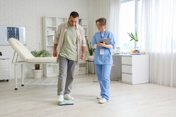 Young man measuring his weight on scales with doctor in clinic