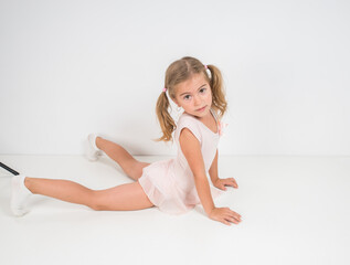 Little girl ballerina in pink dress doing gymnastic exercises.