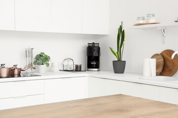 Modern machine with jar of coffee beans and cups on table in kitchen