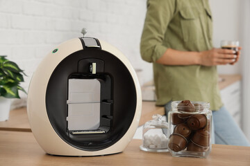 Modern coffee machine with capsules and sugar on table in kitchen