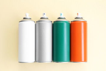 Many spray paint cans on beige background, top view