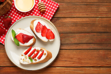 Delicious bruschettas with ricotta cheese, walnuts, mint, strawberries and honey on wooden table, flat lay. Space for text