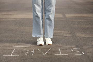 Woman standing on asphalt road with word START. Concept of new beginning