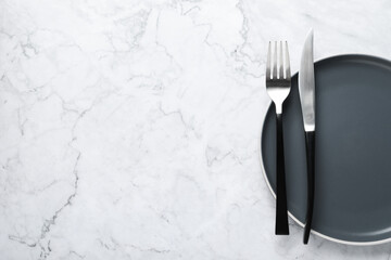 Stylish cutlery and plate on white marble table, top view. Space for text