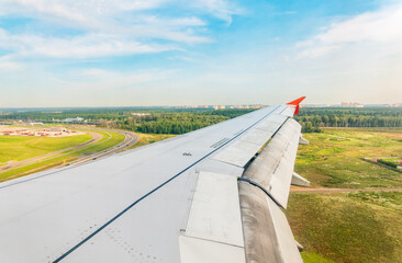 View of airplane wing, blue skies and green land during landing. Airplane window view.