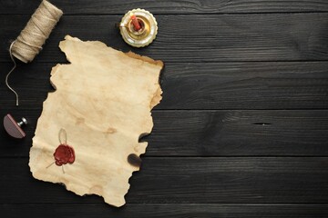 Sheet of old parchment paper with wax stamp, twine and candle on black wooden table, top view....