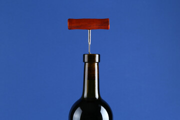 Bottle with corkscrew on blue background, closeup